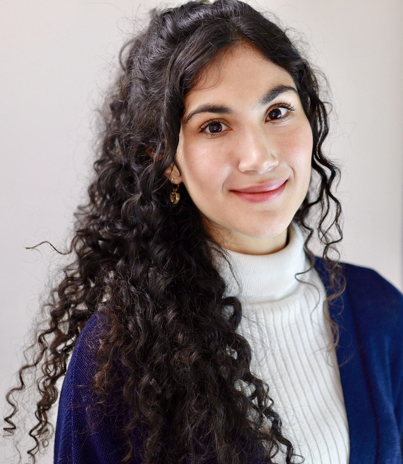 photo of a woman smiling, with curly hair wearing a white turtle neck and a blue cardigan